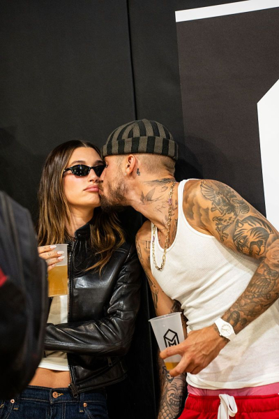 Hailey and Justin Bieber pose at an event. Hailey wears jeans and a leather jacket with a simple sheer white manicure.